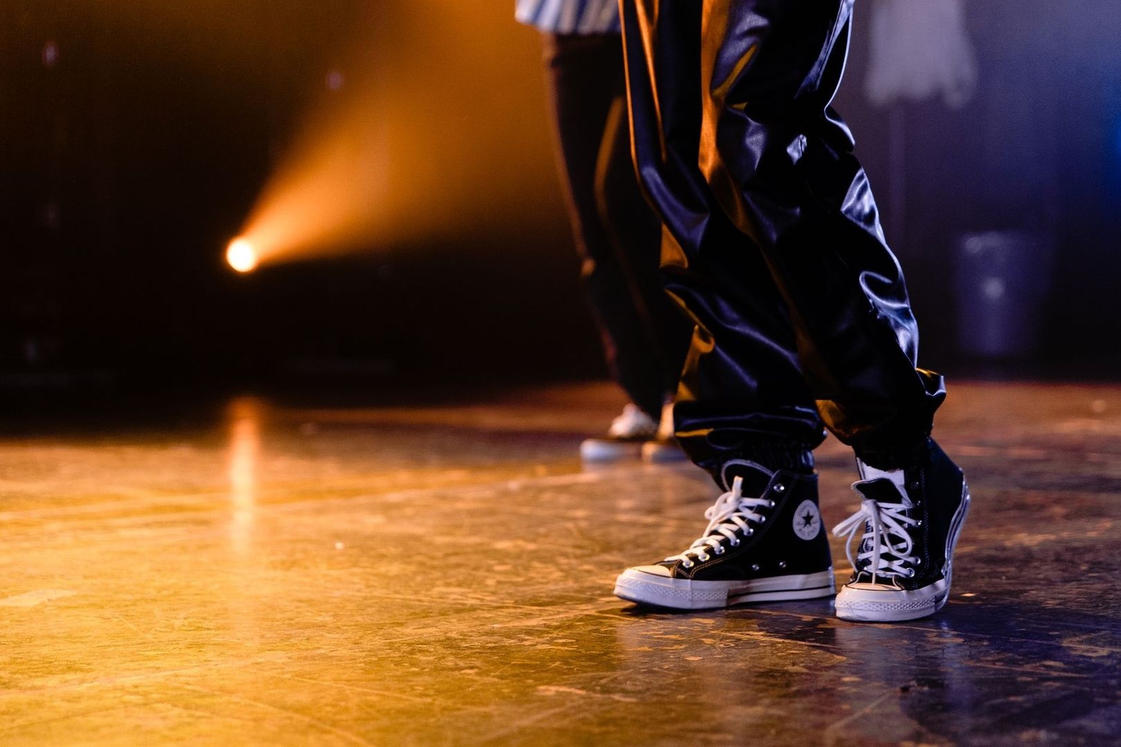 Zwarte sneakers van een danser op een verlichte dansvloer tijdens een battle