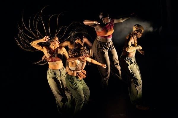 Vier hiphopdansers springen en bewegen op een donker podium